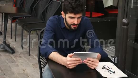 不满的男人在街头咖啡馆用平板电脑玩网络游戏视频的预览图