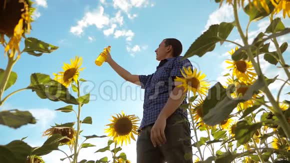 男人手里拿着一个塑料瓶葵花籽油的生活方式站在田野里慢动作视频向日葵视频的预览图