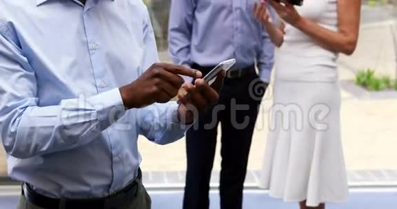 行政人员在同事使用数码平板电脑时使用手机视频的预览图