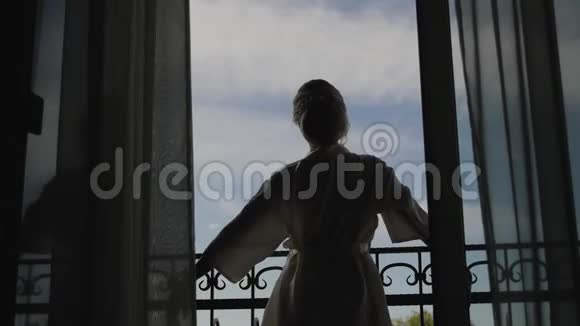 一个年轻的女人走近窗户打开阳台享受着早晨的新娘等待婚礼视频的预览图