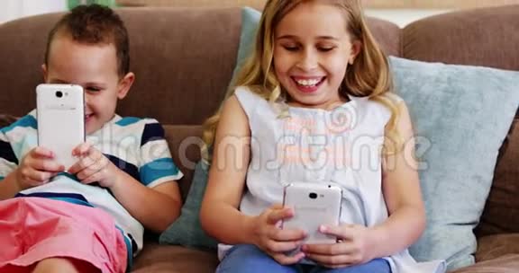 坐在沙发上用手机微笑的男孩和女孩视频的预览图