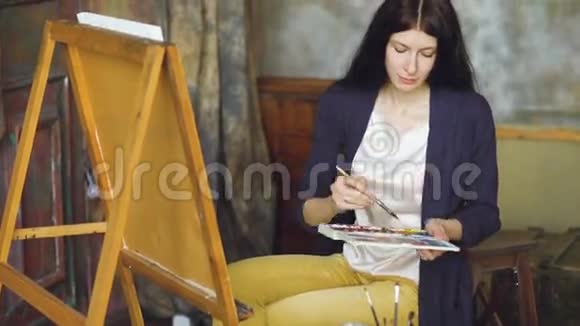 年轻的女画家用水彩画和画架上的画笔画图画视频的预览图