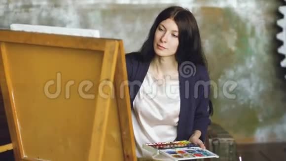 女青年画家在画架上用水彩颜料和画笔画画视频的预览图