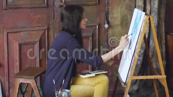 年轻的女画家用水彩画和画架上的画笔画图画视频的预览图