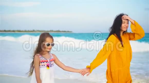 热带海滩上可爱的小女孩和年轻的母亲视频的预览图