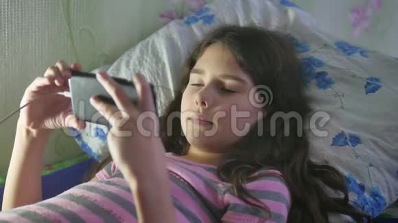 女孩玩智能手机网络游戏社交媒体躺在室内的床上视频的预览图