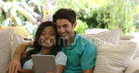 年轻夫妇坐在沙发上在客厅里使用数字平板电脑视频的预览图
