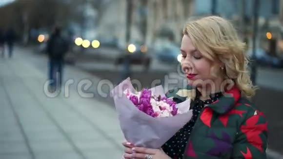一位年轻的金发女子在城市大街上捧着花束视频的预览图