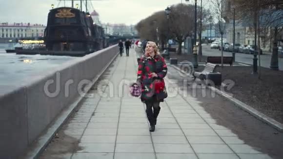 年轻的金发女郎带着花束走在城市街道上视频的预览图