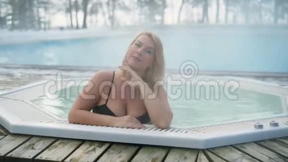 冬季室外浴缸按摩浴缸的年轻金发女子视频的预览图