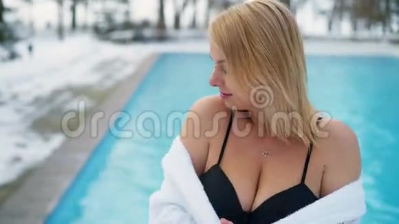 冬季室外游泳池附近穿浴袍的年轻金发女子视频的预览图