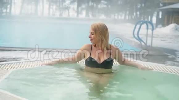 冬季室外浴缸按摩浴缸的年轻金发女子视频的预览图