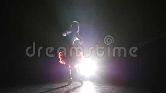 在录音室里一个美丽的女孩在黑暗的背景烟雾剪影上跳拉丁舞视频的预览图