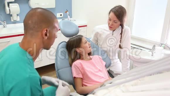 小女孩坐在牙科椅上和牙医和助手说话视频的预览图