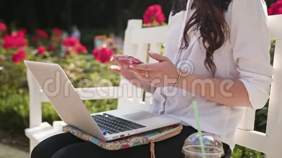 女士坐在公园里用笔记本电脑和电话视频的预览图