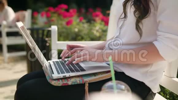 女士坐在公园的长凳上用笔记本电脑视频的预览图