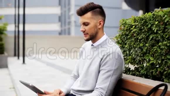 有平板电脑的人坐在城市街头的长椅上视频的预览图