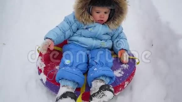 一个快乐的孩子骑在雪管上的雪山上视频的预览图
