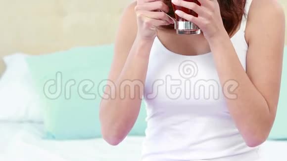 微笑的女人抱着杯子躺在床上视频的预览图