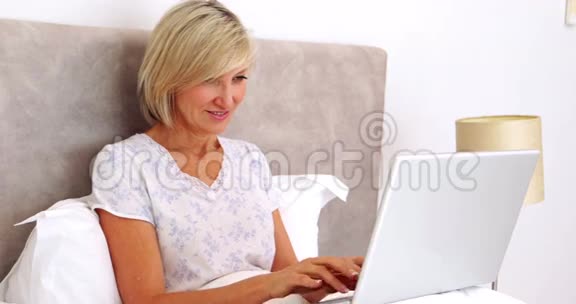 快乐的女人在床上用笔记本电脑视频的预览图