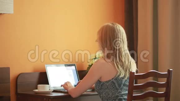 漂亮的女人坐在房子里的桌子上用笔记本电脑工作视频的预览图