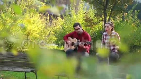 男人一边弹吉他一边和女人一起唱歌一边坐在公园长椅上视频的预览图