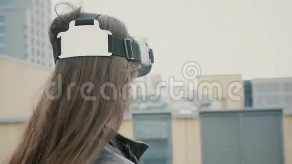 布吕内特的女孩子挥舞着头发在屋顶上使用虚拟现实眼镜4k视频的预览图