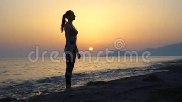 剪影年轻女子在日落时在海滩上练习瑜伽视频的预览图