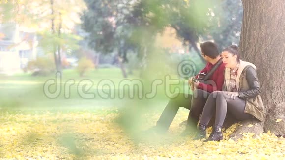 女人唱歌男人弹吉他坐在公园的树上视频的预览图
