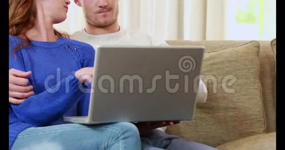 快乐的一对夫妇用笔记本电脑坐在沙发上视频的预览图