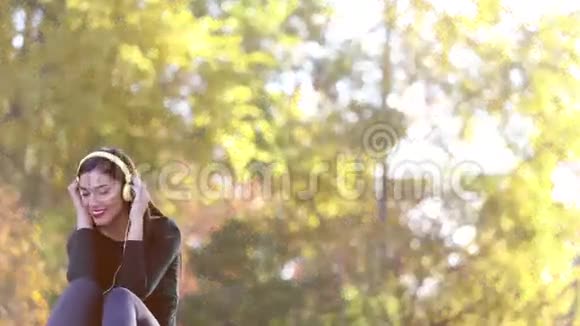 漂亮的黑发女人带着耳机在公园听音乐视频的预览图