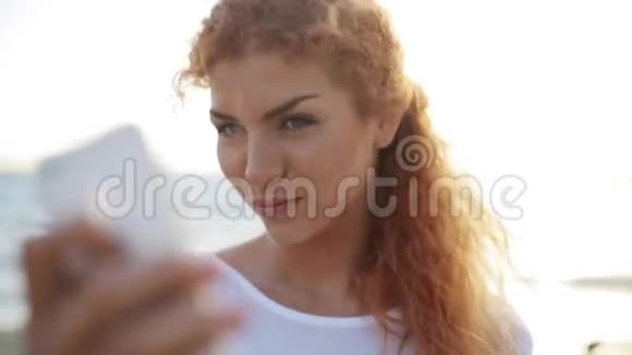 快乐的女人在沙滩上用智能手机自拍视频的预览图