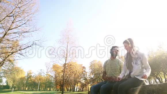 一对年轻的幸福夫妇在公园里用耳机听音乐视频的预览图