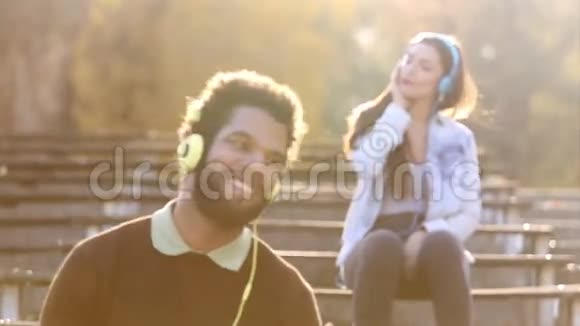 男人和女人在公园里用耳机听音乐视频的预览图