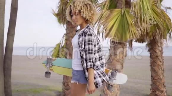 海滩上的年轻女子带着滑板视频的预览图