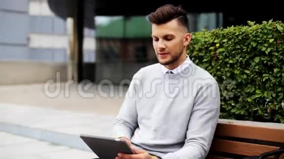 有平板电脑的人坐在城市街头的长椅上视频的预览图