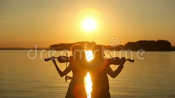 小提琴二重奏在湖上日落时分男人和女人在大自然中拉小提琴视频的预览图