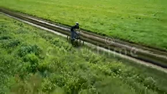 年轻人骑自行车在乡村公路上穿过绿色和黄色的田野视频的预览图