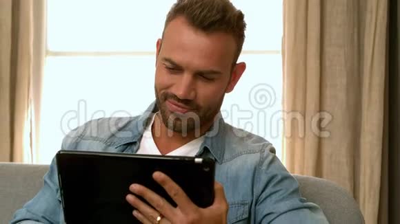 微笑的男人在沙发上用平板电脑视频的预览图