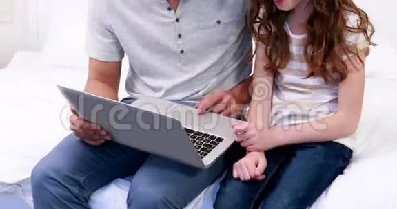 微笑的父亲和女儿使用笔记本电脑视频的预览图