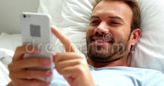 男人微笑着在床上使用智能手机视频的预览图