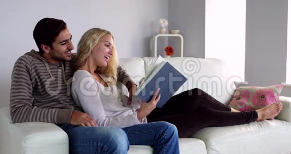 可爱的年轻夫妇一起在沙发上看书视频的预览图