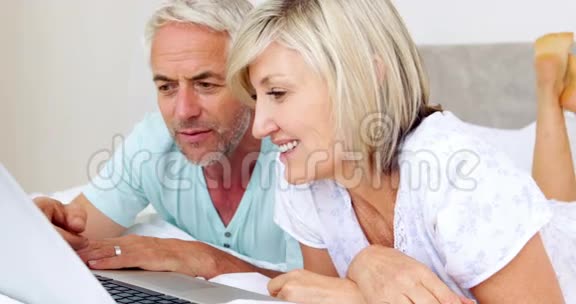 快乐的一对夫妇一起躺在床上用笔记本电脑视频的预览图