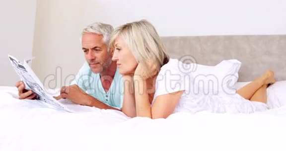一对躺在床上一起看报纸的夫妇视频的预览图
