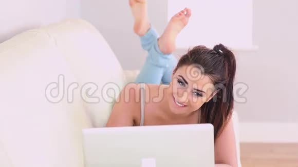 在沙发上用笔记本电脑的漂亮黑发女人视频的预览图