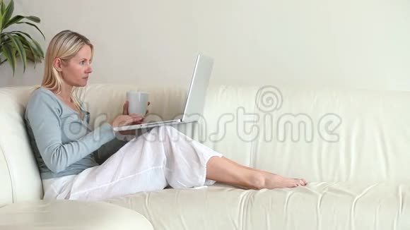 坐在沙发上的女人正在她的笔记本电脑上打字视频的预览图
