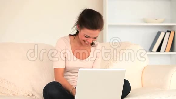 快乐的黑发女人坐在沙发上用手提电脑放松视频的预览图