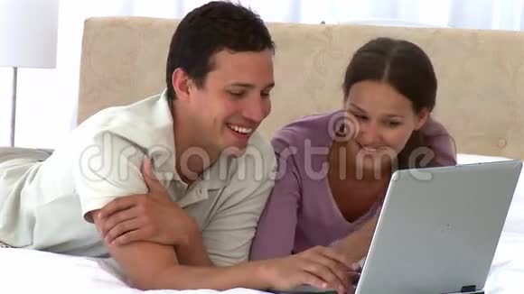 快乐的一对夫妇躺在床上看着笔记本电脑视频的预览图