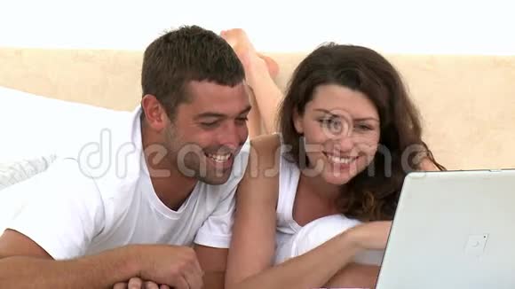 快乐的一对夫妇用笔记本电脑躺在床上视频的预览图