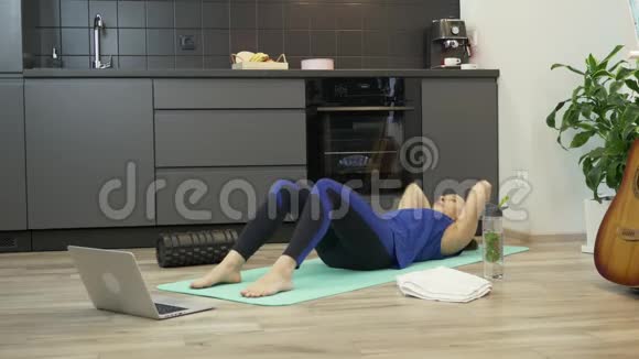 健身女孩在家厨房做腹部运动使用笔记本电脑上的在线培训应用程序年轻女子体育运动视频的预览图